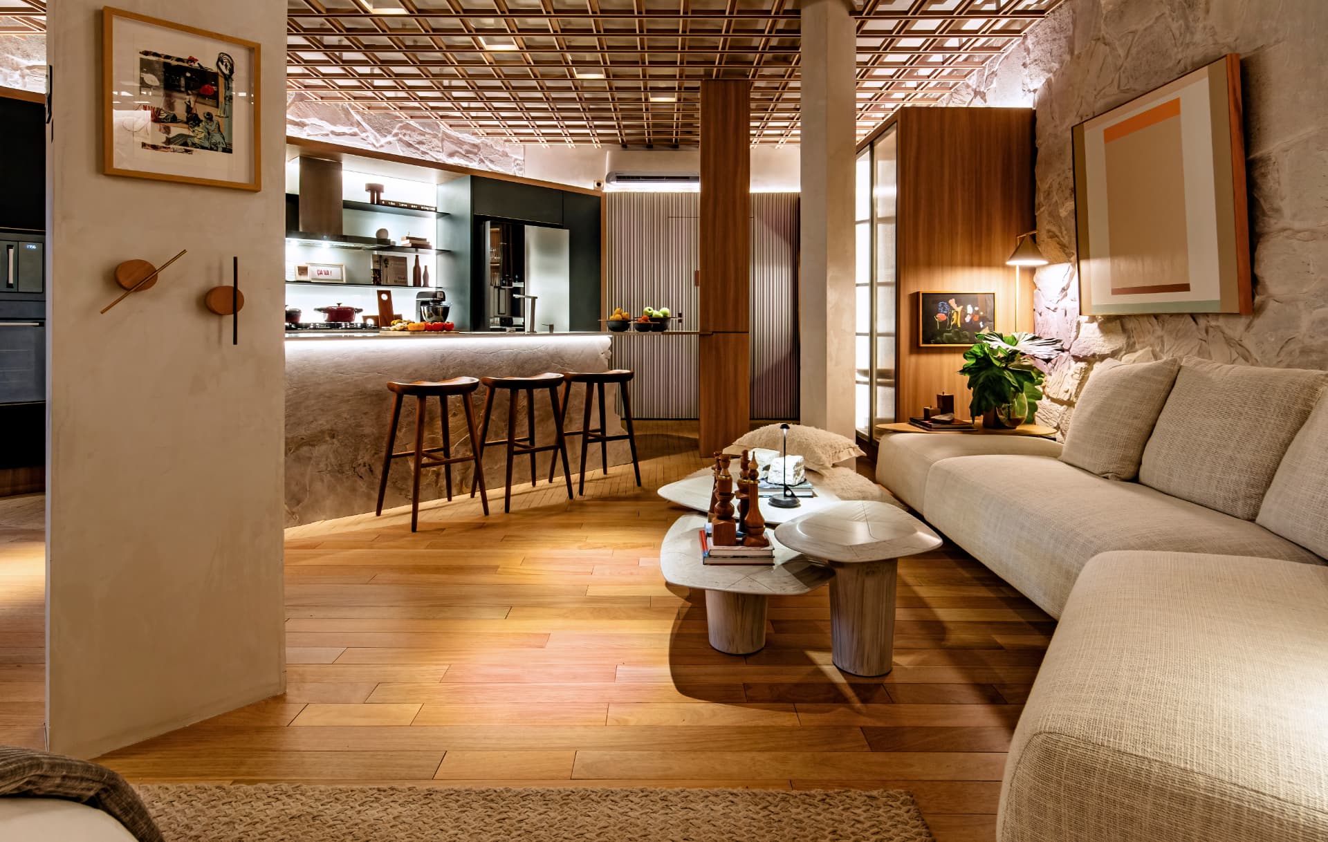 Sala de estar integrada à cozinha com pedra natural, madeira e iluminação quente