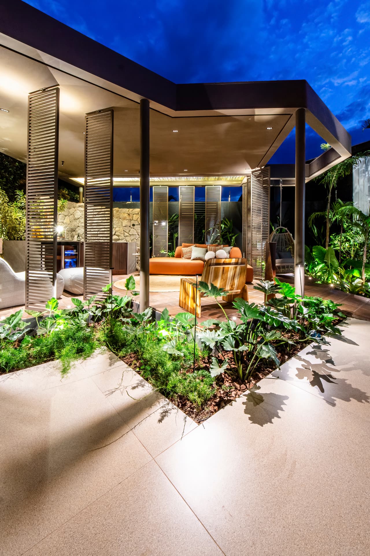 Área externa noturna com paisagismo exuberante e iluminação cênica