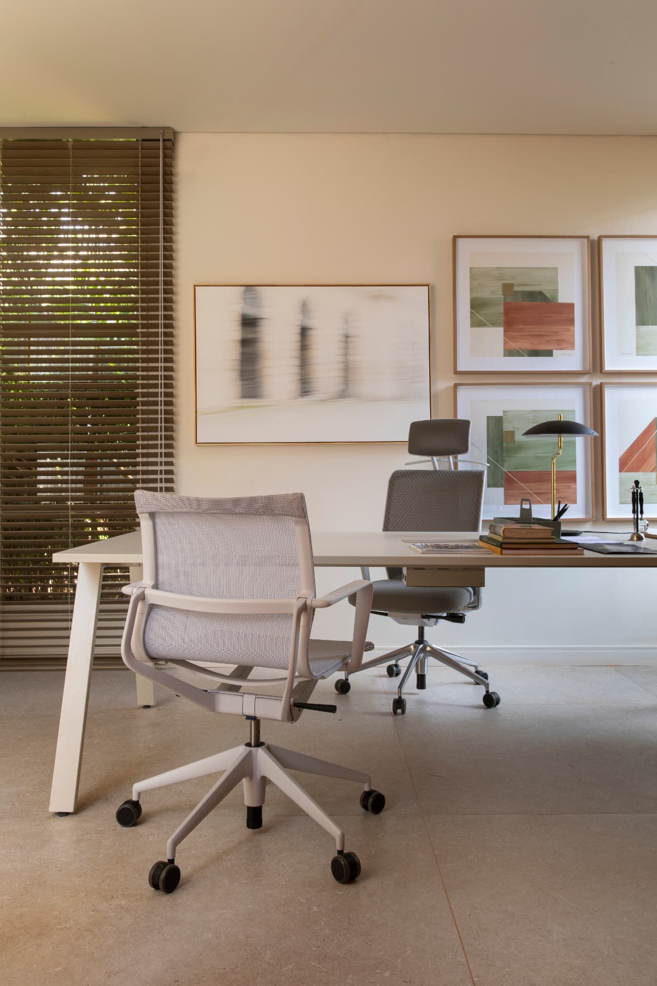 Home office com mesa clara, cadeiras ergonômicas e conjunto de quadros