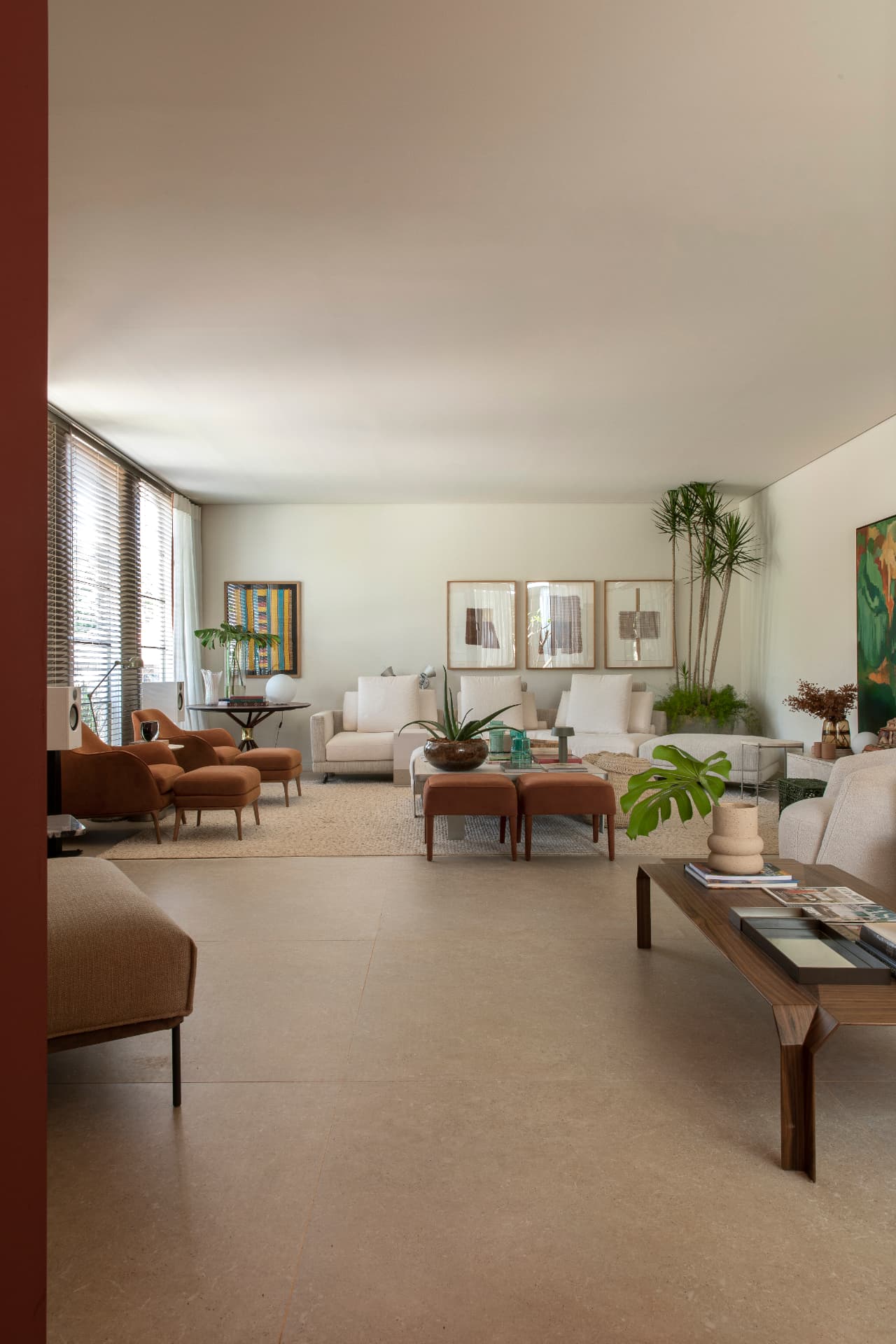 Living amplo com sofás claros, poltronas terracota e porcelanato de grande formato