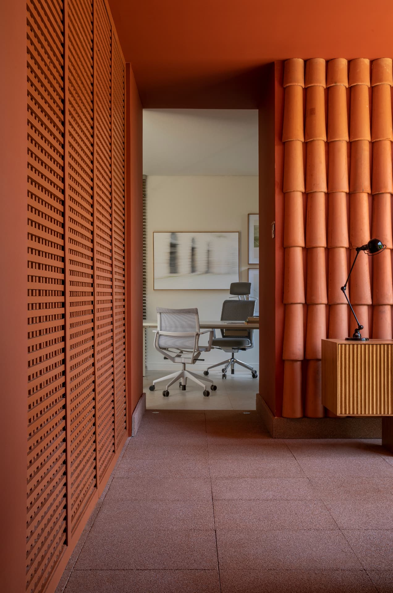 Corredor terracota com muxarabi, parede de telhas cerâmicas e vista para o escritório