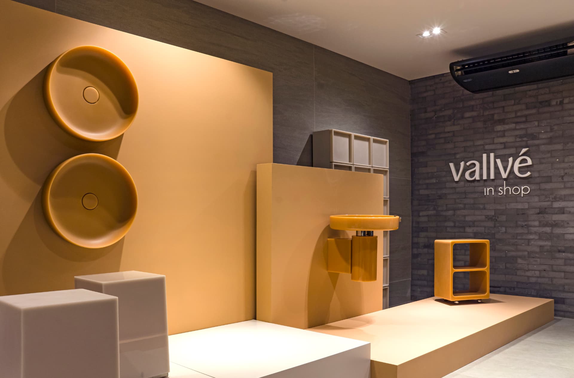 Showroom Vallvé na Casa Cor com cubas e móveis em tom mostarda sobre bases claras