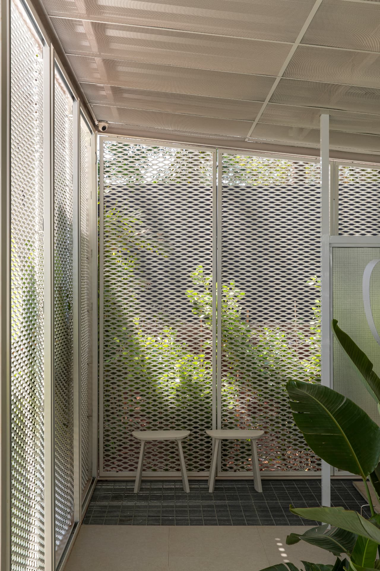 Área de duchas com banquetas brancas e painéis de metal expandido com vista para o verde
